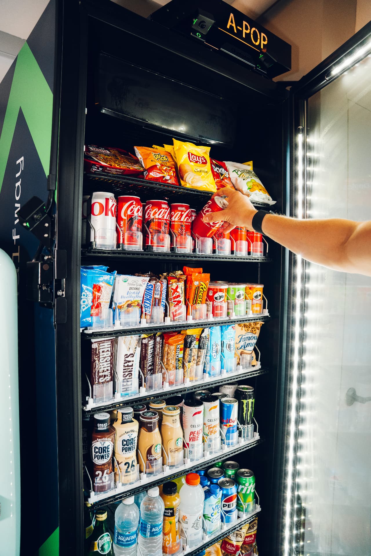 Smart cooler A-POP con productos variados y una mano tomando una bebida